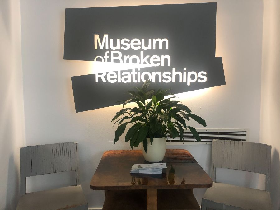 A neon sign behind a table and chairs reading Museum of Broken Relationships