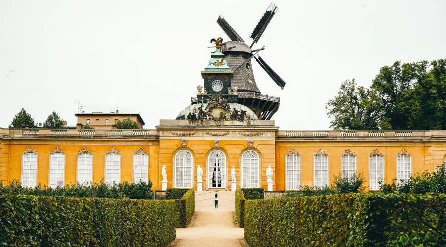 Yellow palace a wooden windmill in the background and garden hedges in the fore ground