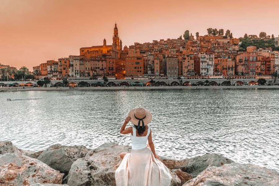 A girl wearing a hat overlooking the water towards the town of Menton