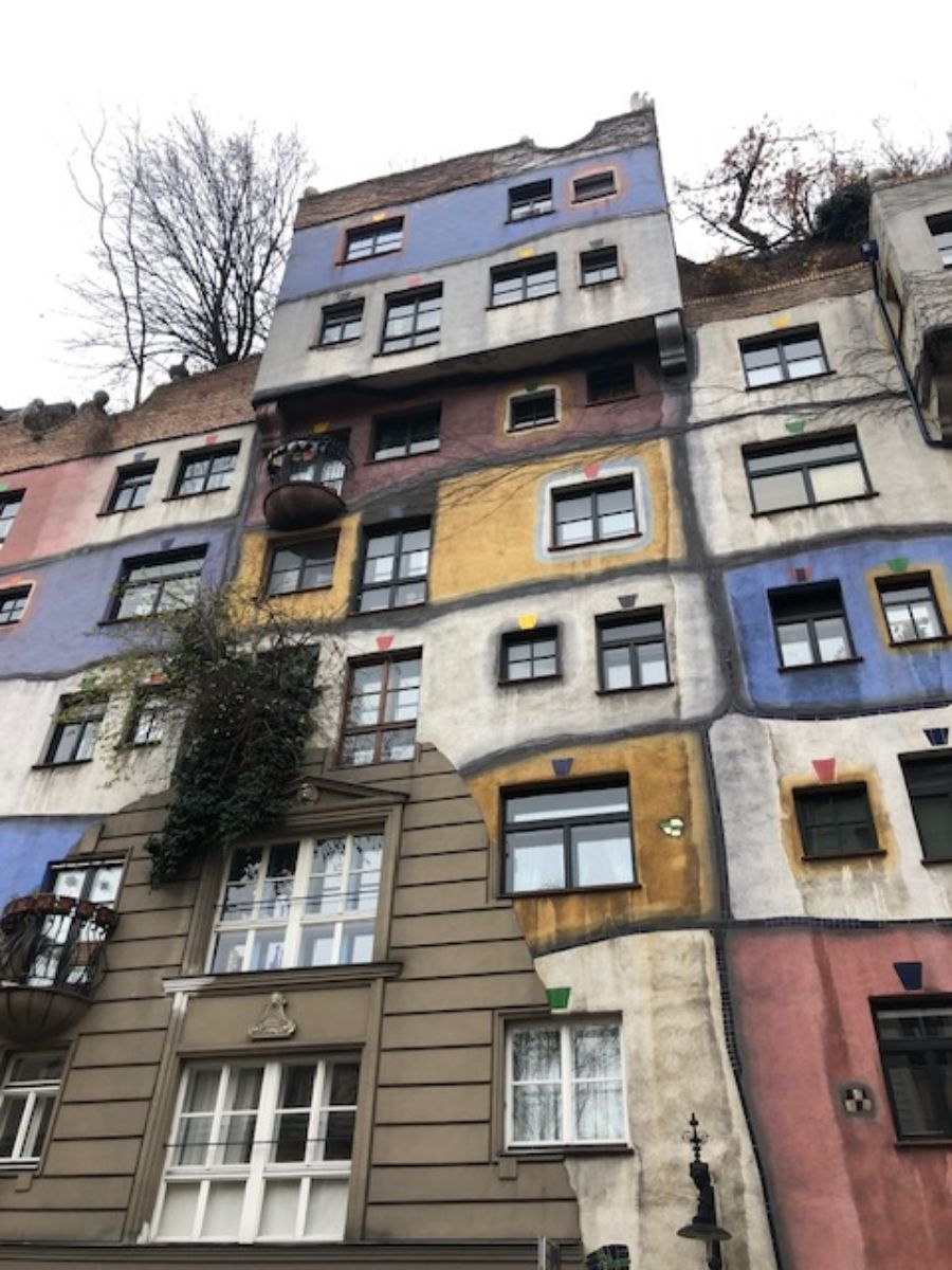 The unique and colorful façade of the Hundertwasser House in Vienna, showing the building's distinctive irregular forms, vibrant paintwork, and integrated natural elements like trees and shrubs